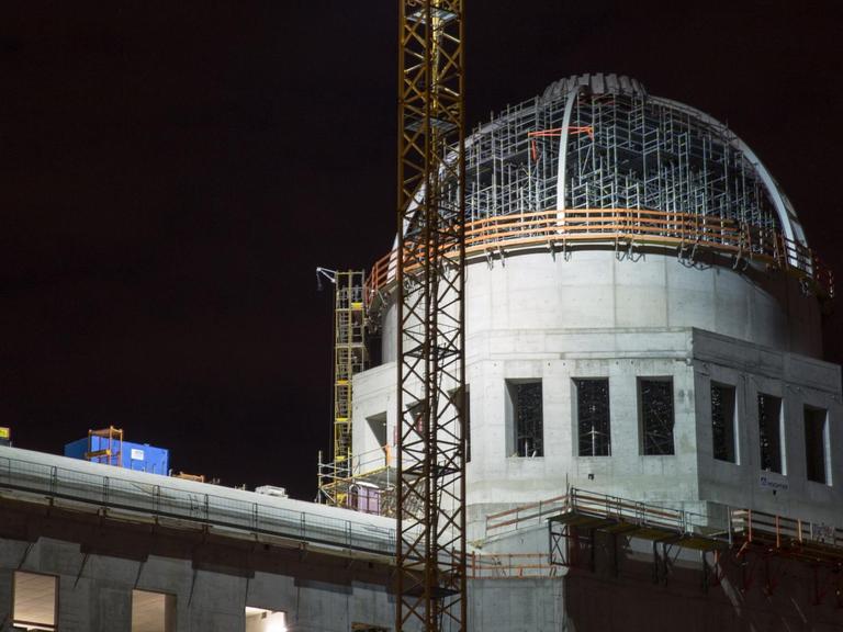 Die Kuppel des Rohbaus des Berliner Schlosses, das den Namen Humboldt-Forum trägt, in Berlin. Es ist Nacht, im Vordergrund ein Baukran.