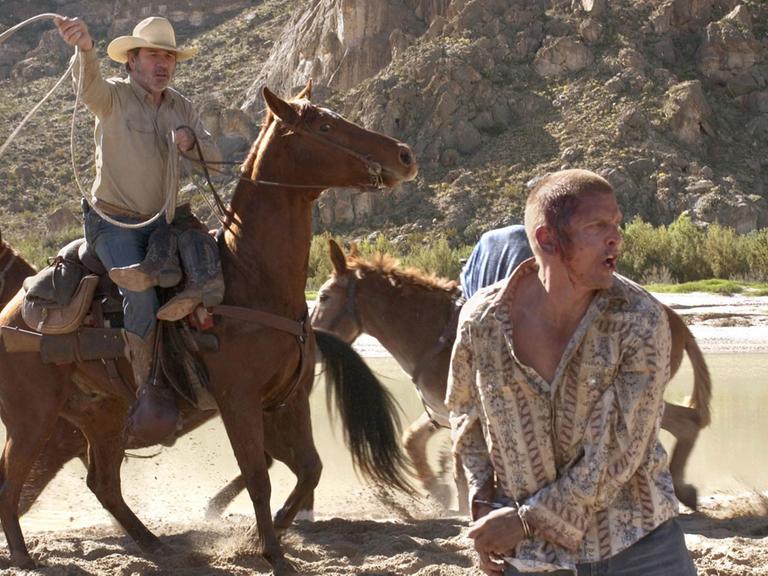 Filmszene aus Three Burials: Pete Perkins (l, gespielt von Tommy Lee Jones) versucht auf einem Pferd sitzend Mike Norton (Barry Pepper) mit einem Lasso zu fangen.