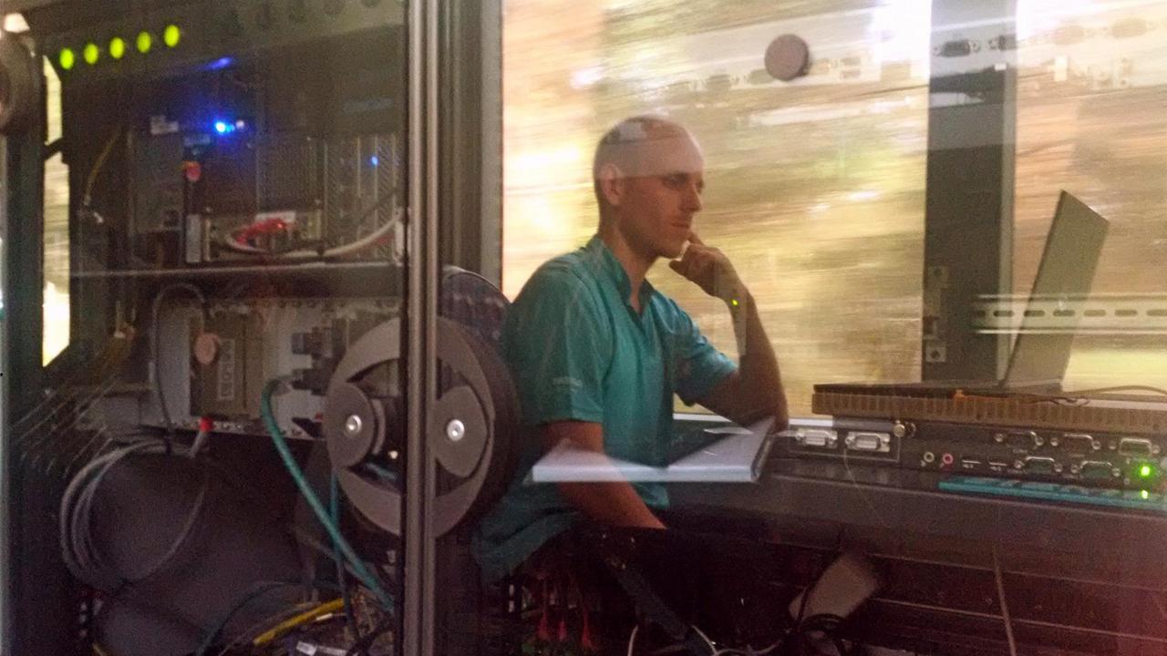 In einer Straßenbahn sitzt ein Mann hinter einer Glasscheibe und blickt auf einen Laptop.