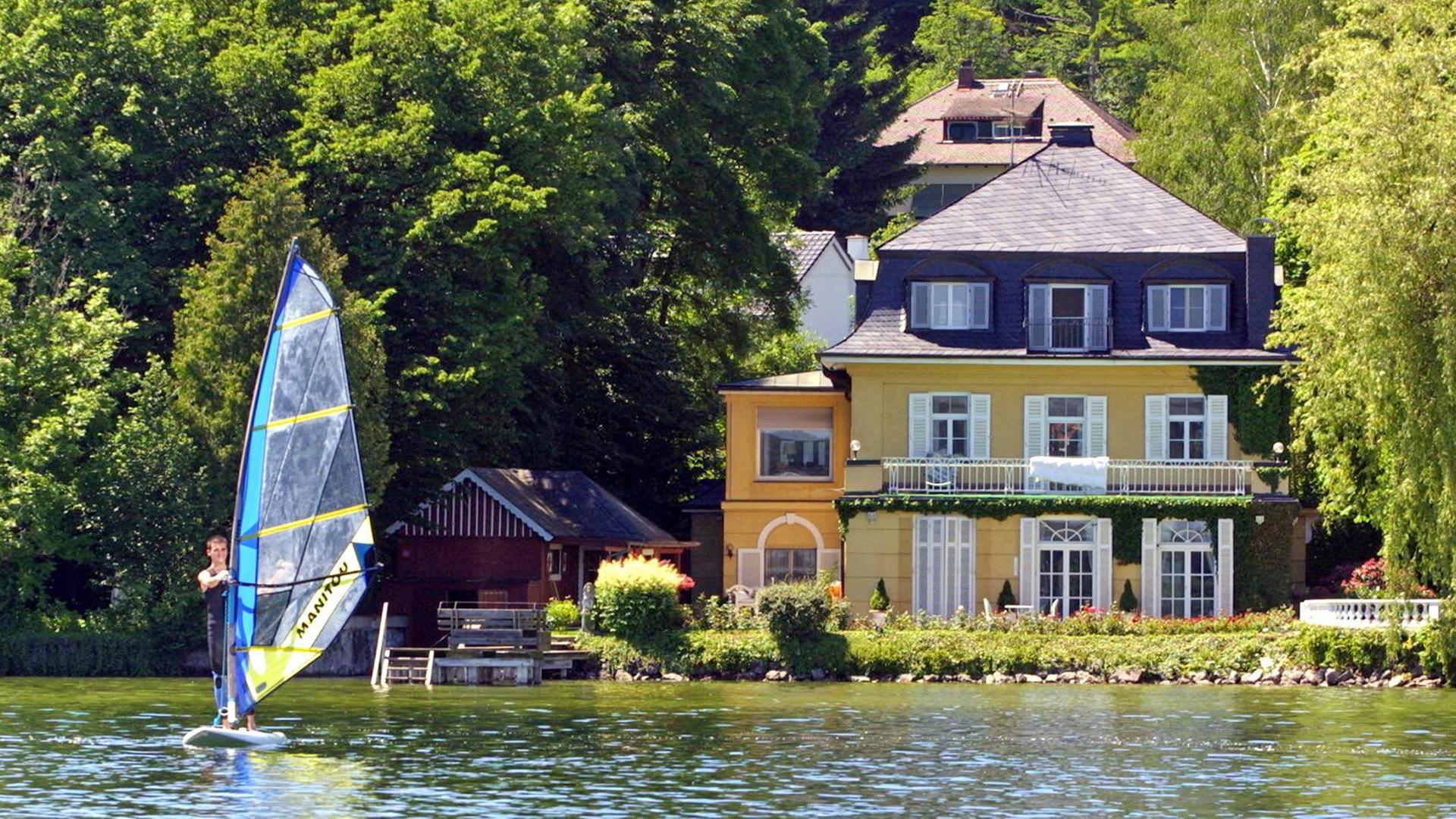Eine Villa am Starnberger See. Davor ein Surf-Brett.