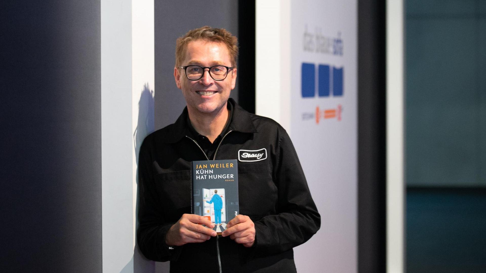 Jan Weiler lehnt an einer Wand mit seinem neuen Buch.
