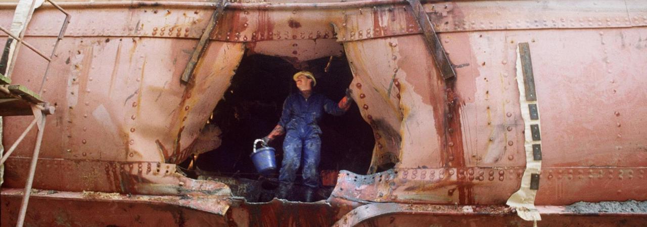 Ein Arbeiter begutachtet das Loch im Rumpf des Greenpeace-Schiffes "Rainbow Warrior", auf dem Rump ist das Wort "Peace" zu lesen.