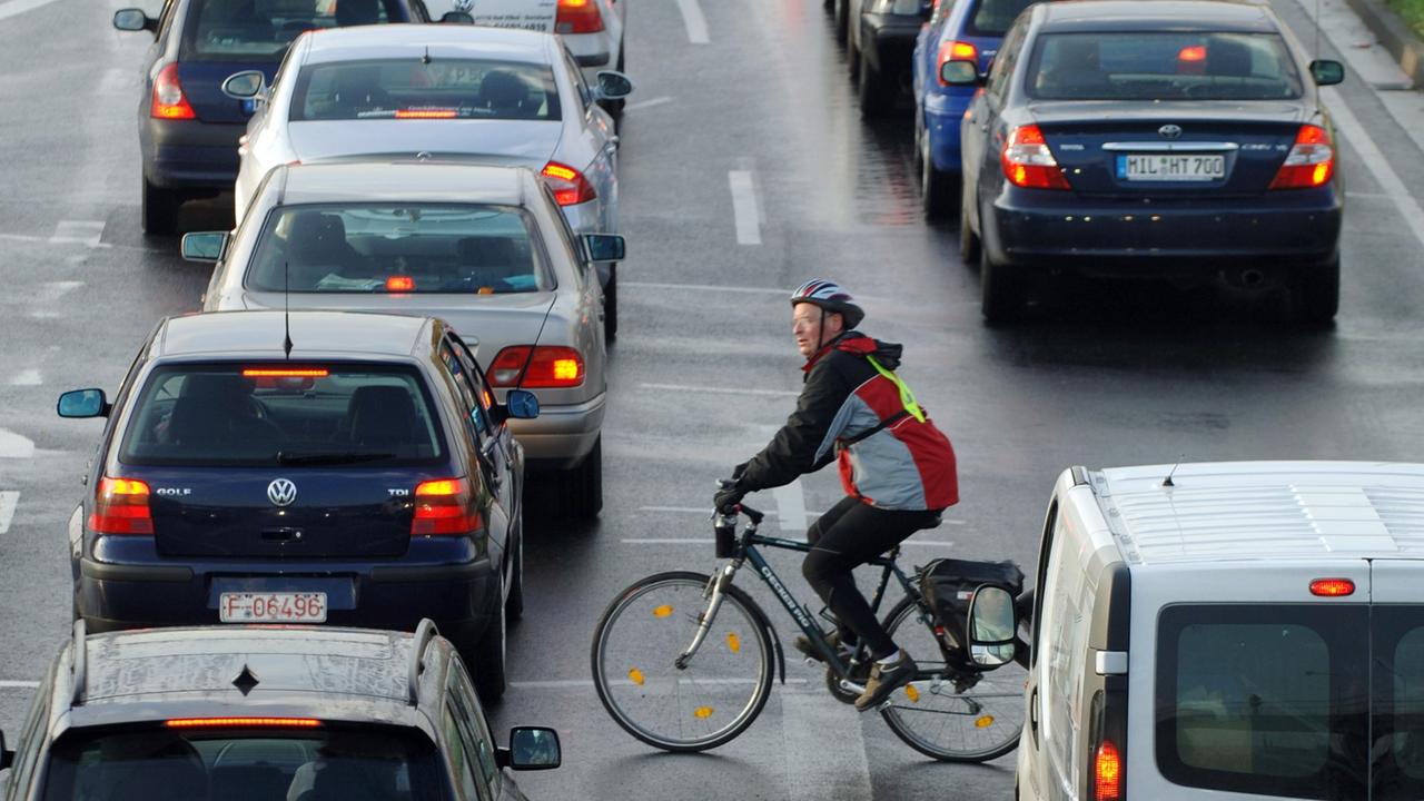 Ein Fahrradfahrer fährt zwischen Autos im Berufsverkehr vorbei.