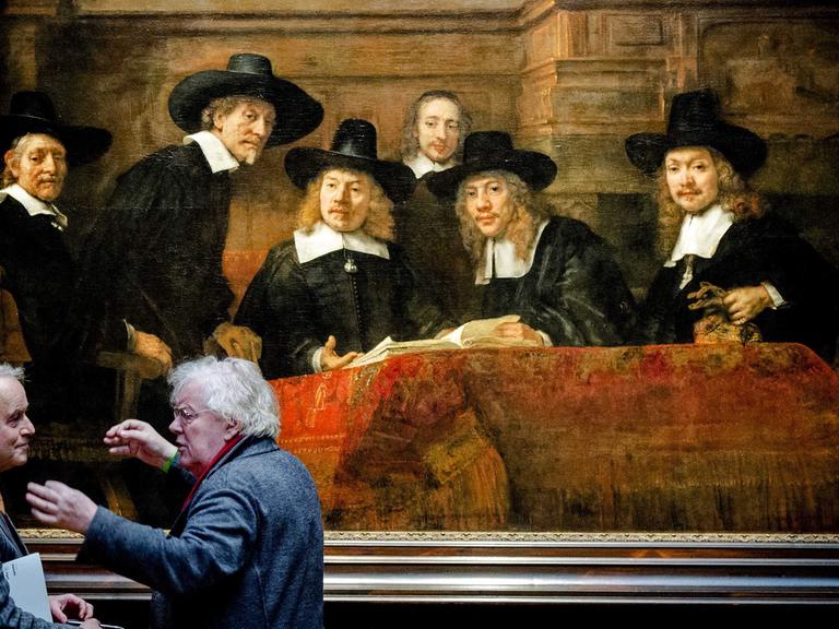 Zwei Männer diskutieren vor Rembrandts "The Steelmasters", das in der Ausstellung "Der späte Rembrandt" im Amsterdamer Reichsmuseum gezeigt wird.