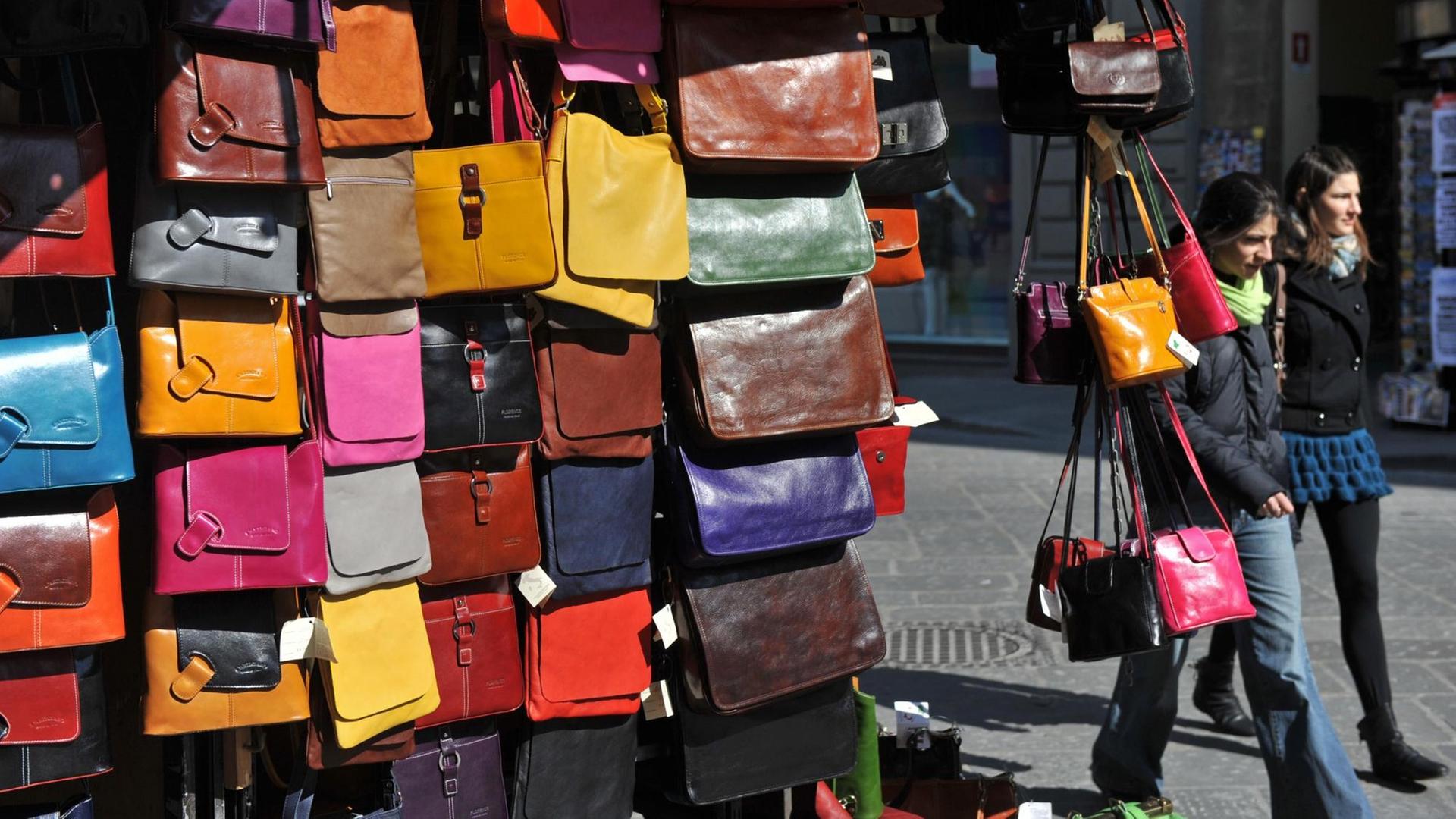 Zwei Frauen gehen am Montag (08.03.2010) in Florenz an einem Stand mit Leder-Handtaschen in verschiedenen Farben vorbei. Foto: Andreas Gebert dpa/lby | Verwendung weltweit