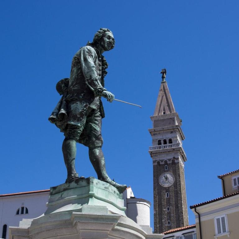 Blick auf die Statue des Geigers, dessen Geigenbogen zu einer Kirche im Hintergrund weist.