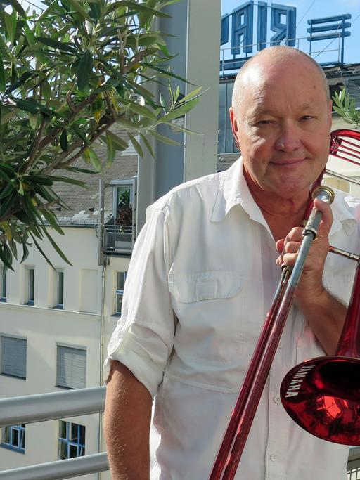 Der schwedische Jazzmusiker Nils Landgren steht mit seinem Markenzeichen, der roten Posaune, auf der Dachterasse von Deutschlandfunk Kultur.