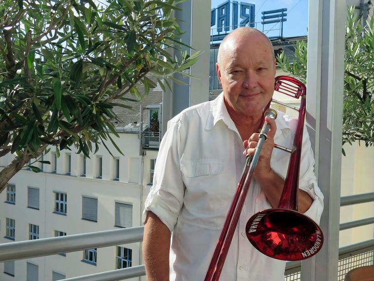 Der schwedische Jazzmusiker Nils Landgren steht mit seinem Markenzeichen, der roten Posaune, auf der Dachterasse von Deutschlandfunk Kultur.