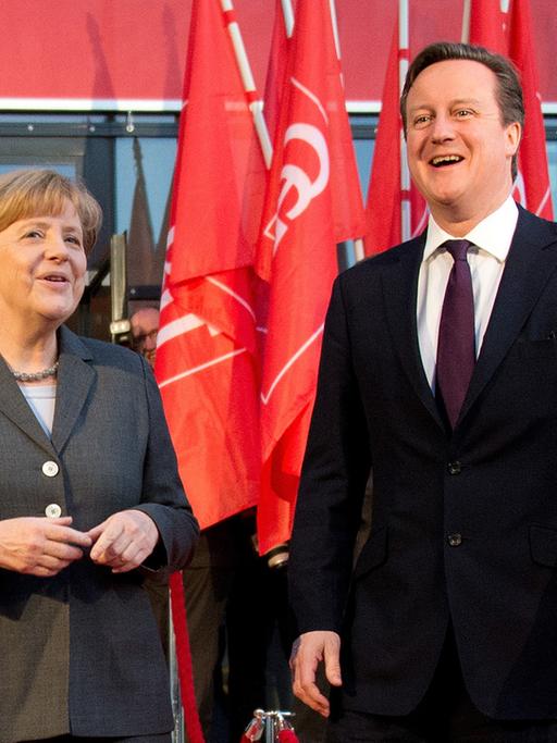 Angela Merkel und David Cameron stehen lächelnd vor roten Flaggen der Computermesse CeBIT in Hannover