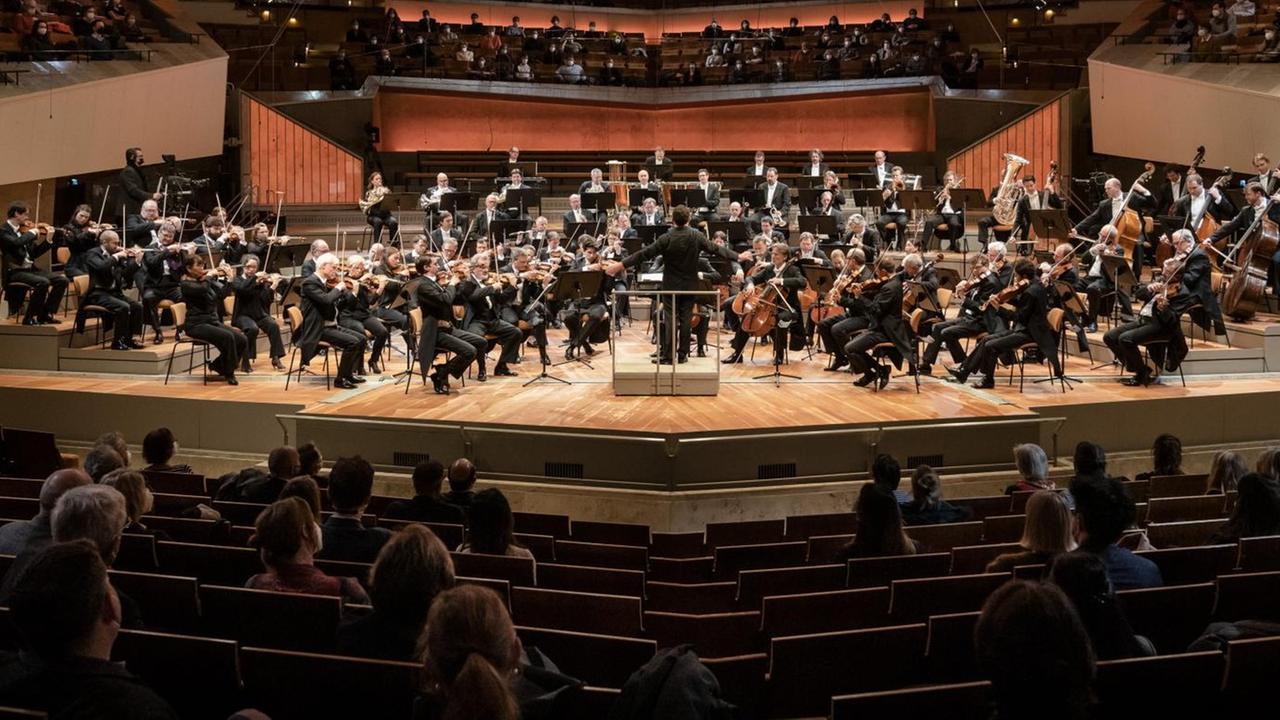 Eine Bühne im Scheinwerferlicht, dort stehen viele Menschen mit Instrumenten.