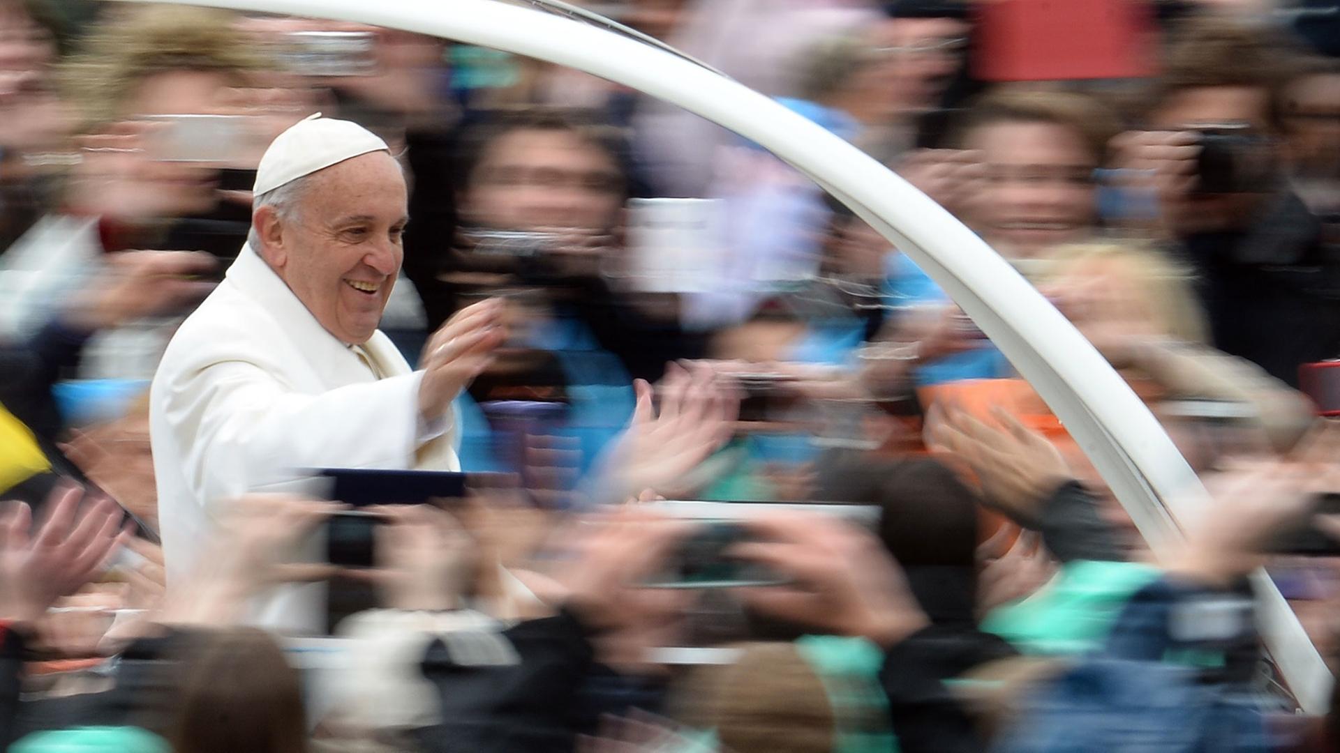 Papst Franziskus grüßt Menschen auf dem Petersplatz im Rom von seinem Papamobil aus.