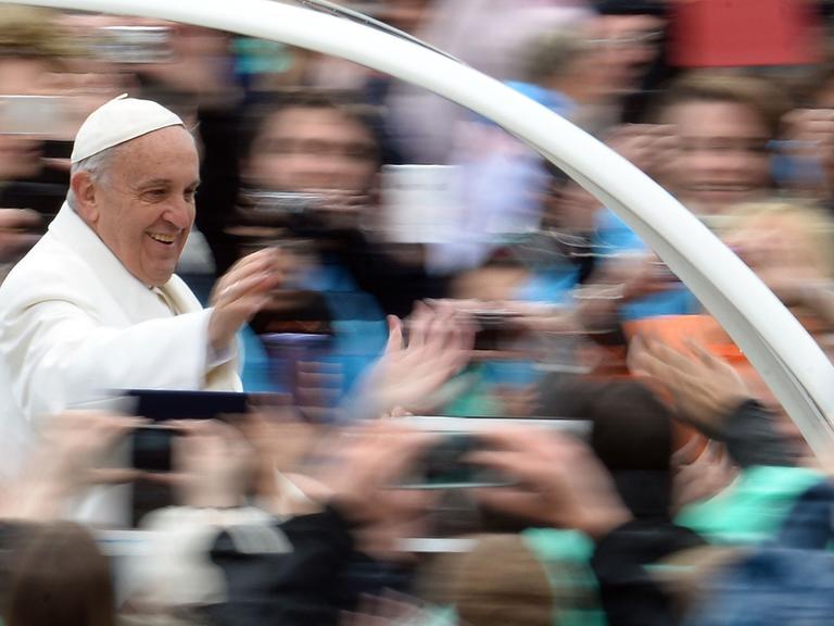 Papst Franziskus grüßt Menschen auf dem Petersplatz im Rom von seinem Papamobil aus.