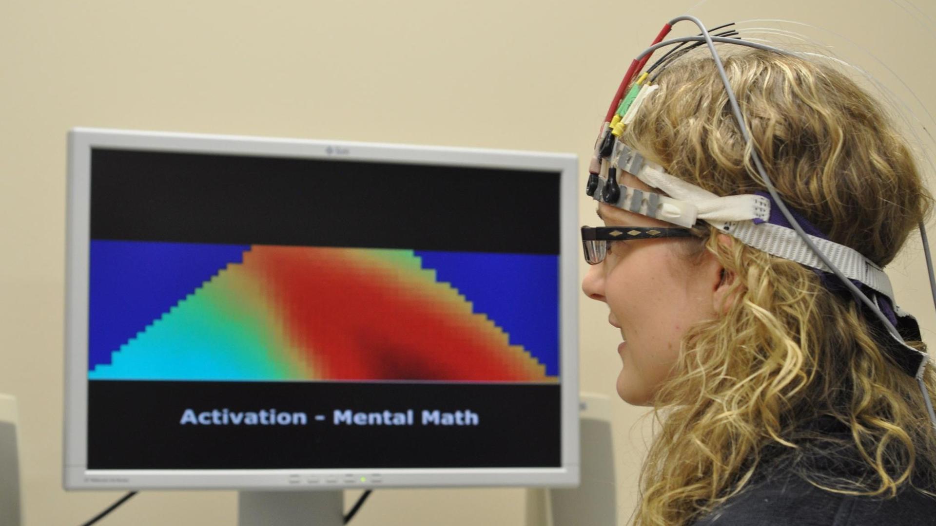 Eine Frau mit einem Stirnband, dass die Gehirnaktivität misst, vor einem Bildschirm