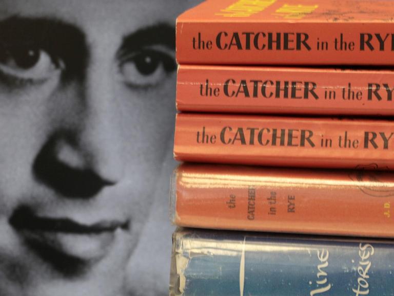Das Gesicht des Schriftstellers J.D.Salinger neben aufgestapelten Büchern seines Klassikers "Der Fänger im Roggen".