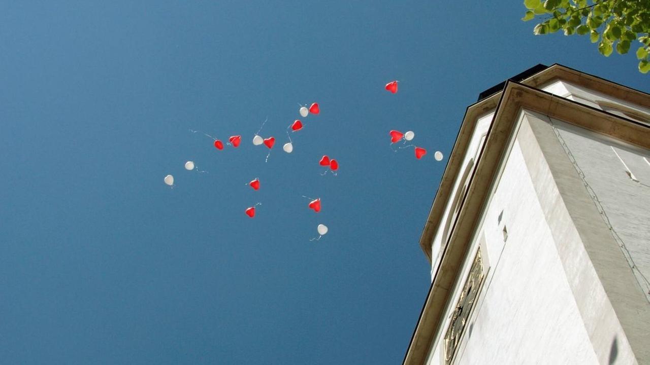 Rote und weiße Ballons steigen neben einer Kirche in den blauen Himmel
