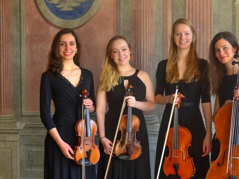 Die vier Musikerinnen stehen in einem historischen Raum in edler, schwarzer Konzertrobe.
