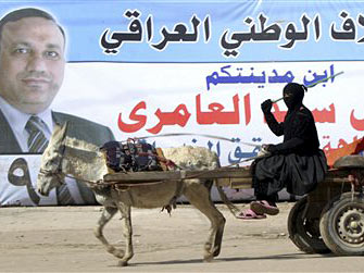 Eine verschleierte Frau fährt in einem Eselskarren in Nadschaf an einem Wahlplakat des Kandidaten Qais al-Amari vorbei.