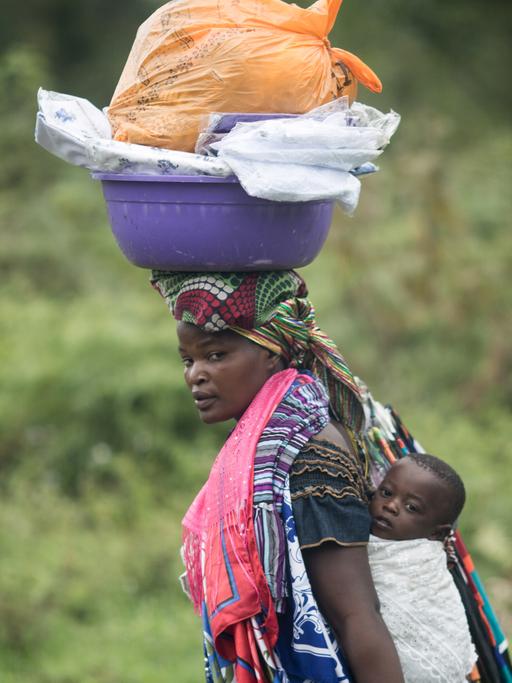 Eine Frau trägt im Distrikt Nyiragongo bei Goma in der Demokratischen Republik Kongo ihr Baby auf dem Rücken und Waren auf dem Kopf.