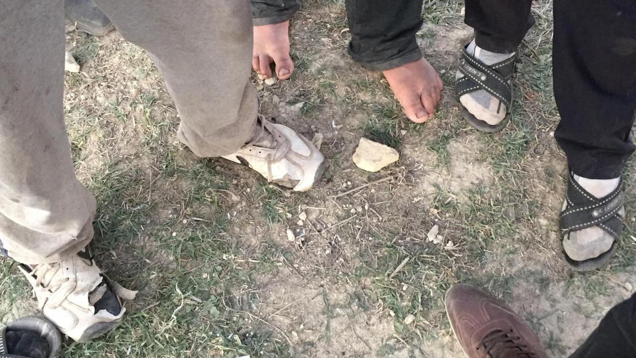 Blick auf die Füße von mehreren Männern mit zerschlissenen Schuhen oder barfuß