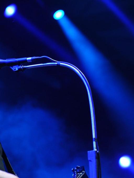 Farin Urlaub ist von der Seite zu sehen, wie er im schwarzen T-Shirt Gitarre spielt und ins Mikrofon singt. Hinter ihm strahlen Scheinwerfer blaues Licht vor schwarzem Hintergrund.