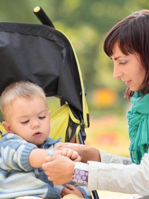 Eine Mutter kümmert sich in einem Park um ihren Sohn im Kinderwagen.