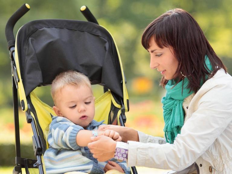 Eine Mutter kümmert sich in einem Park um ihren Sohn im Kinderwagen.