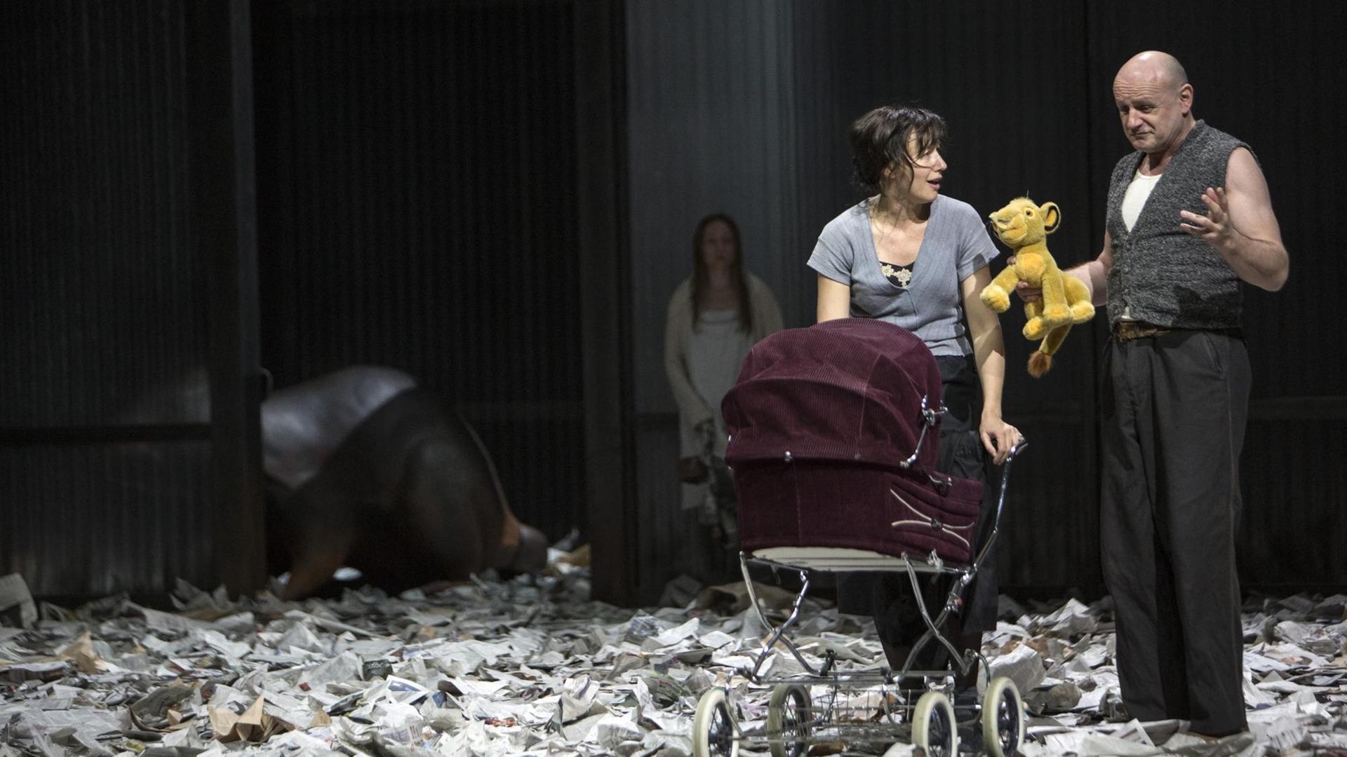 Eine Frau und ein Mann schieben einen Kinderwagen, der Mann (Oliver Stokowski als Herr John) hält einen Plüschbabylöwen in der Hand.