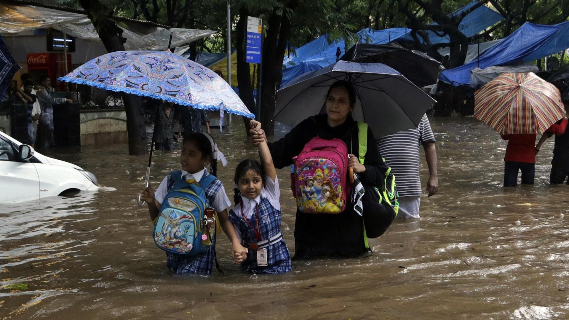 Eine Mutter mit zwei Schulkindern geht am 29.08.2017 in Mumbai (Indien) über eine überflutete Straße. Heftige Regenfälle haben am 29.08.2017 Teile der Stadt lahmgelegt.