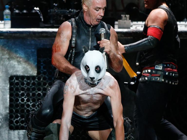 Till Lindemann, Sänger der Band Rammstein sitzt beim Wacken Open-Air Festival auf dem Keyboarder der Band, Flake Lorenz, der sich eine Panda-Maske aufgesetzt hat