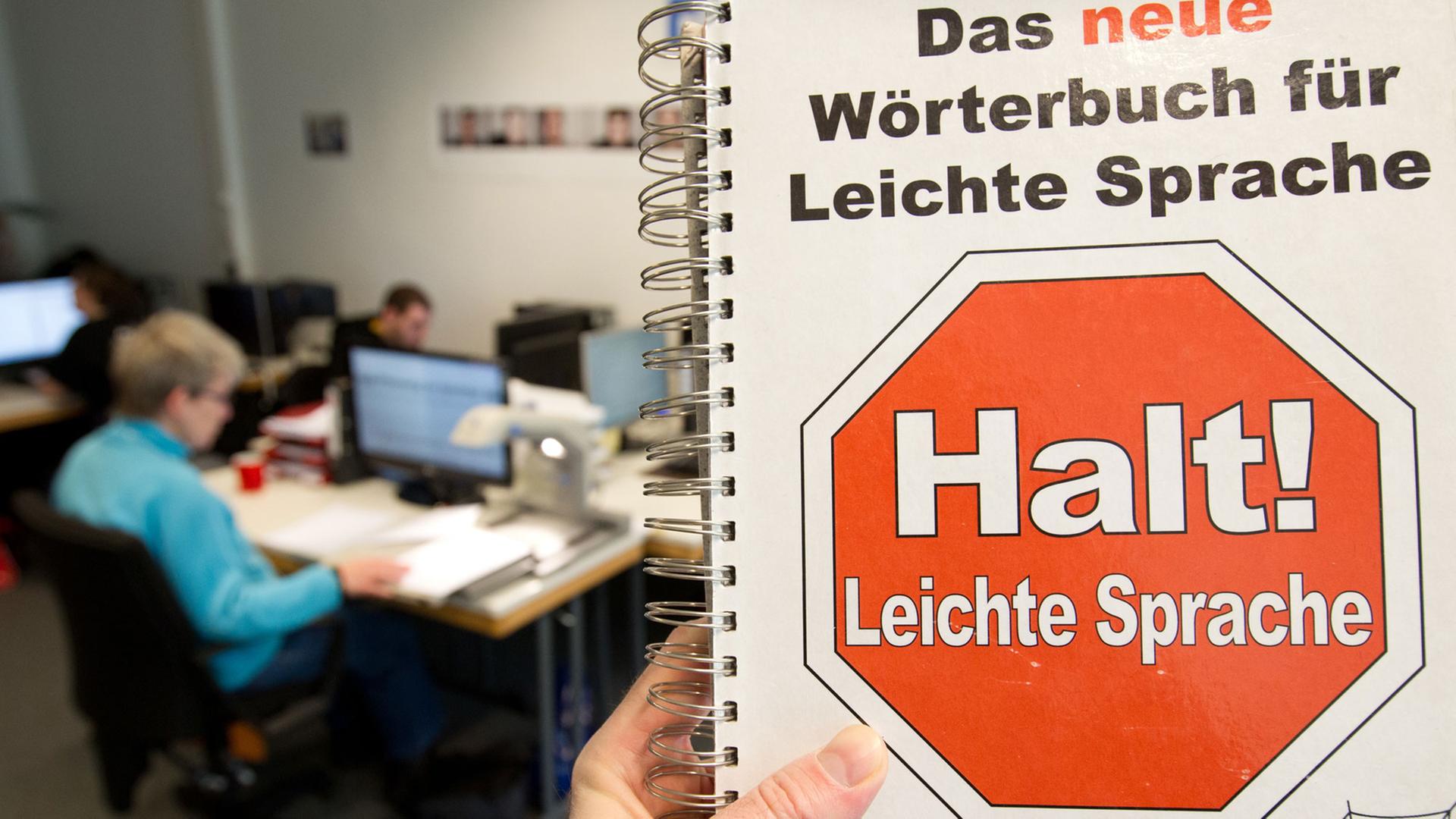 Eine Mitarbeiterin vom Büro für Leichte Sprache sitzt in der Hochschule Osnabrück vor einem Computermonitor - fotografiert mit einem "Wörterbuch für Leichte Sprache".