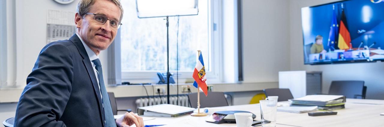 Schleswig-Holsteins Ministerpräsident Daniel Günther während der Videokonferenz mit den Regierungschefs der Länder und Bundeskanzlerin Merkel. Günther sitzt in einem Büro und schaut auf einen Großbildschirm.