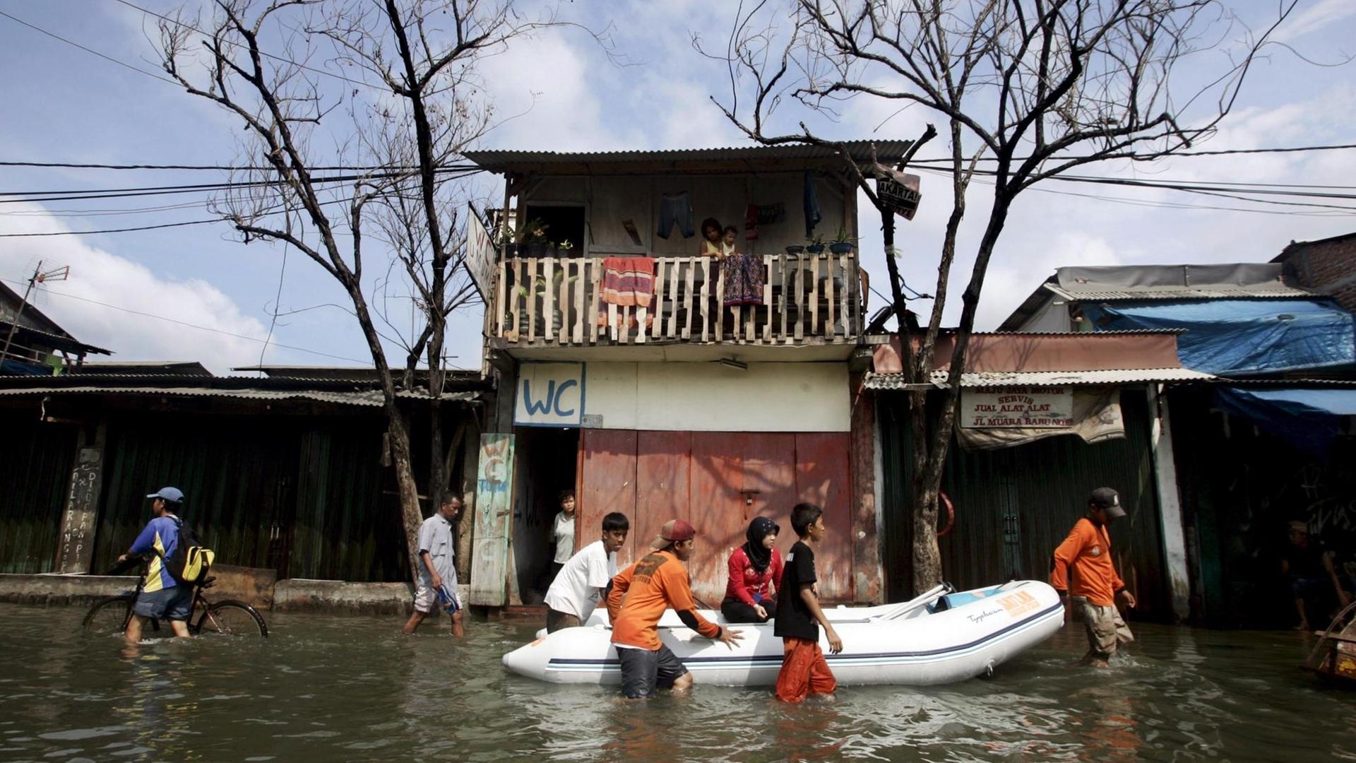 Menschen in der Stadt Jakarta ziehen ein Boot durch eine überschwemmte Straße. 