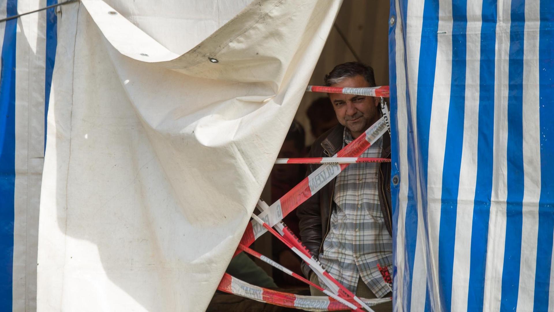Ein Mann schaut über eine Absperrung aus einem blau-weiß gestreiften Zelt