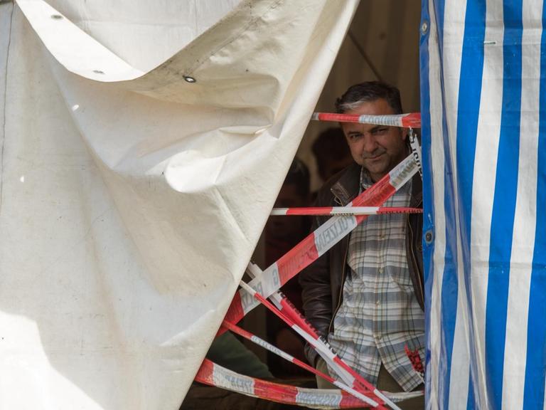 Ein Mann schaut über eine Absperrung aus einem blau-weiß gestreiften Zelt