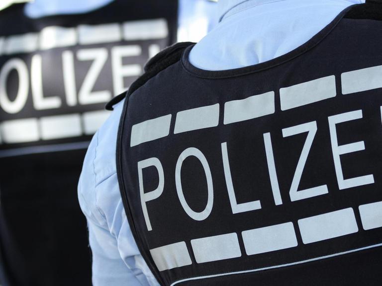Die Rückansicht von zwei Polizistenwesten zeigen die Aufschrift "Polizei"