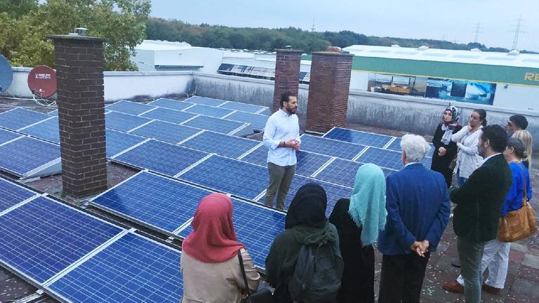 Ein muslimische Gruppe aus Frauen und Männern schaut sich eine Solaranlage auf dem Dach an.