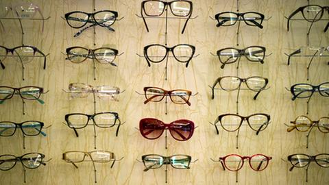Auf einem Display eines Optiker-Geschäftes sind Brillen in Reihen ausgestellt.
