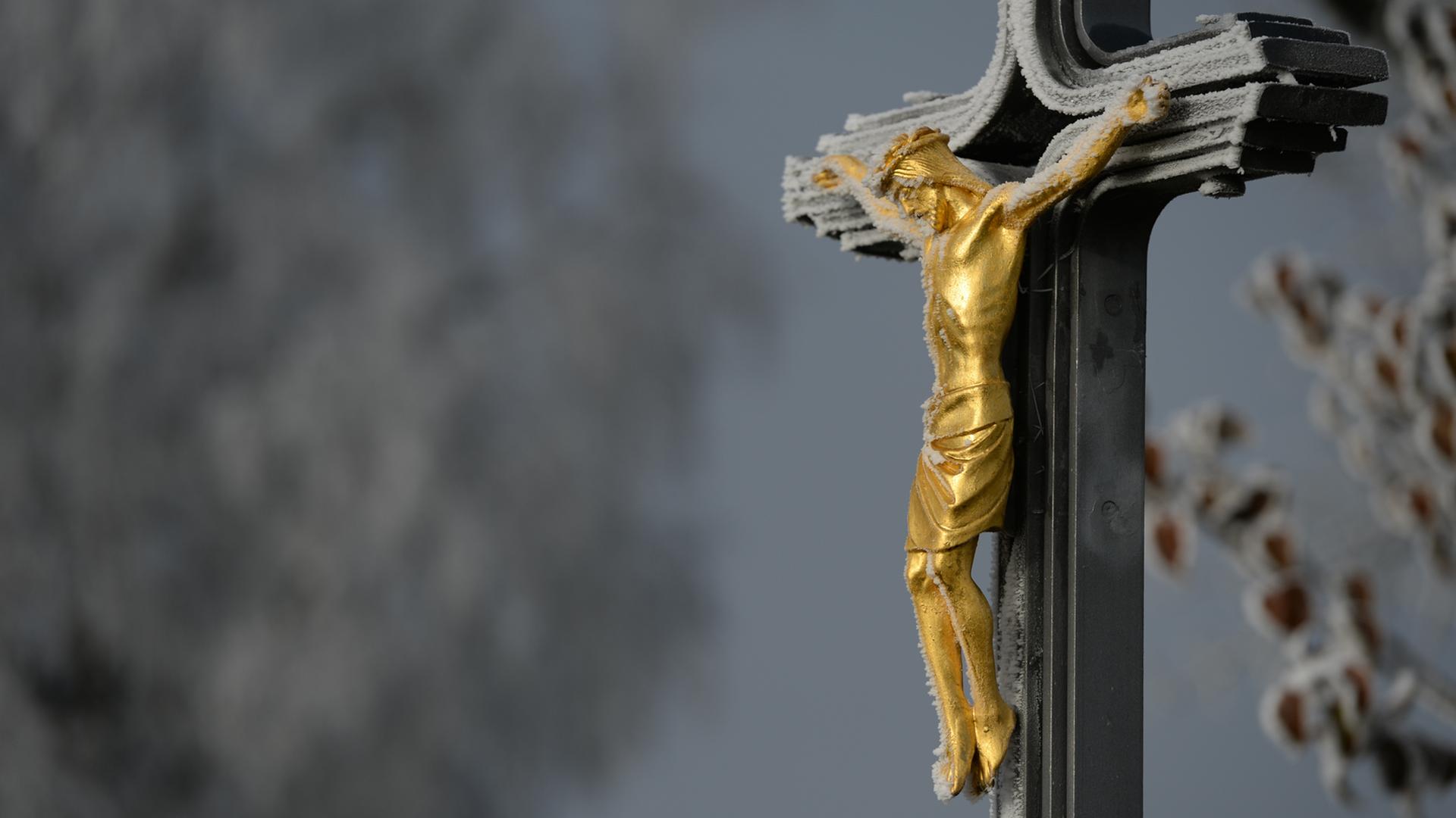 Ein Metallkreuz mit einer goldenen Christusfigur mit einem dünnen Schleier von Frost