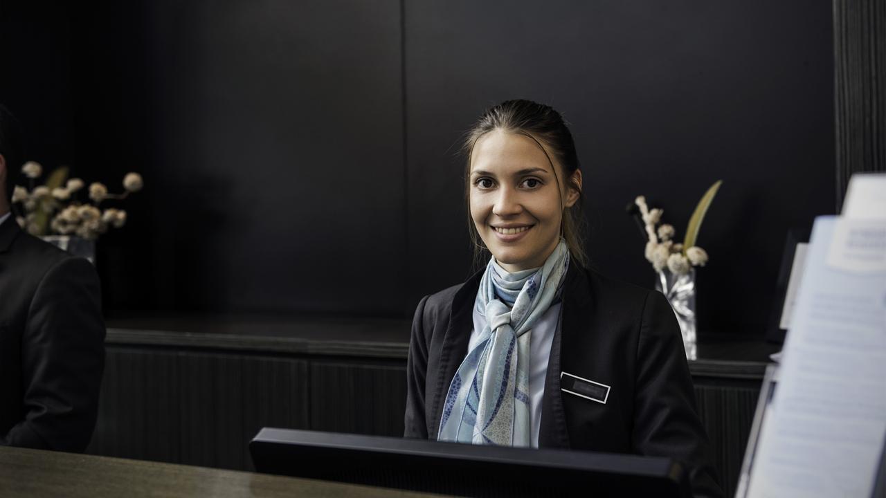 Eine junge Frau sitzt lächelnd hinter einer dem Tresen einer Hotelrezeption.