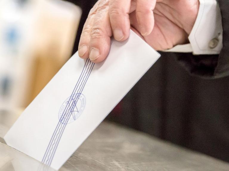 Ein Hand steckt einen Wahlschein in eine Wahlurne.
