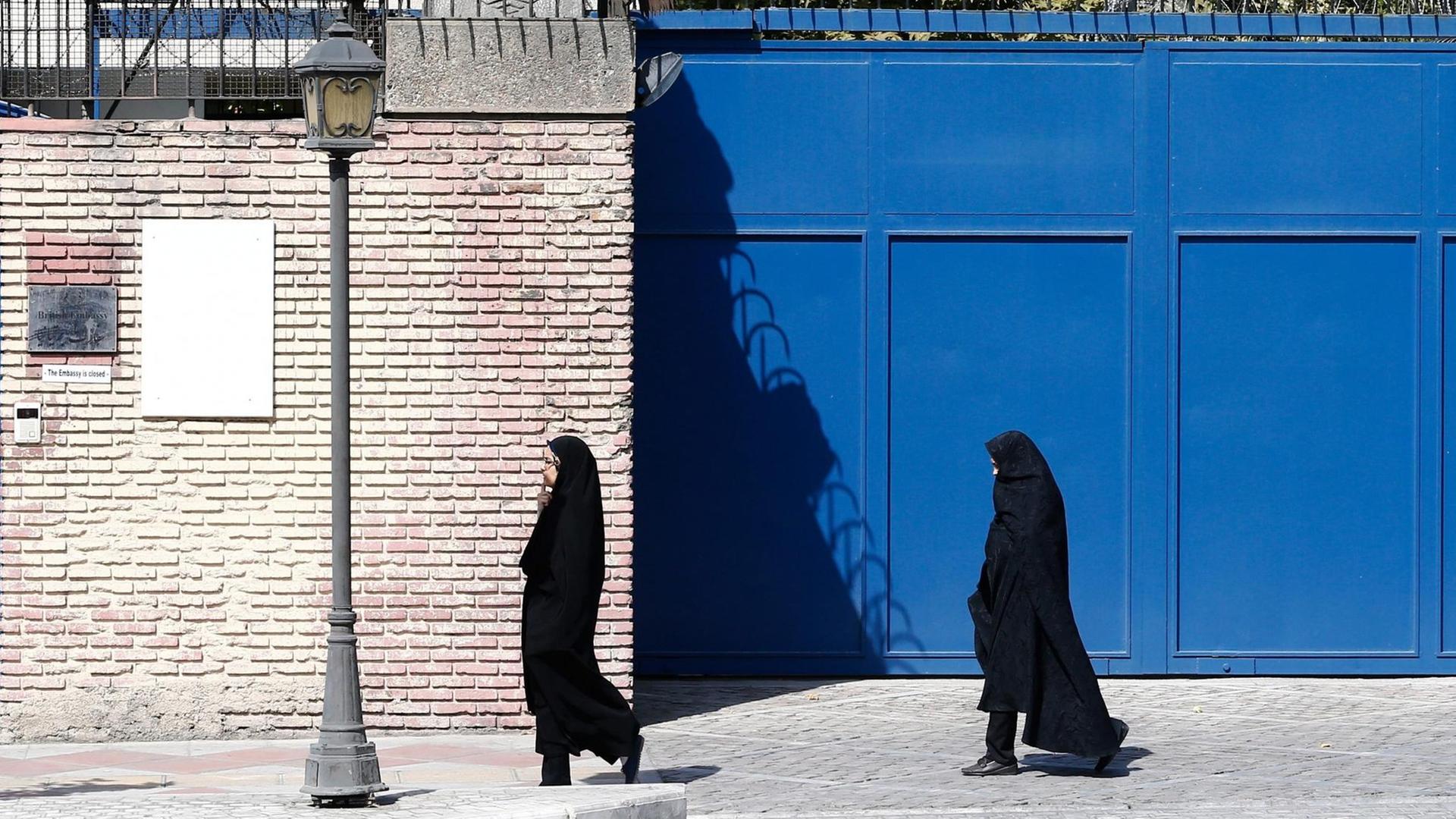 Zwei verschleierte Frauen gehen vor dem Eingang der britischen Botschaft in Teheran einen Weg entlang.