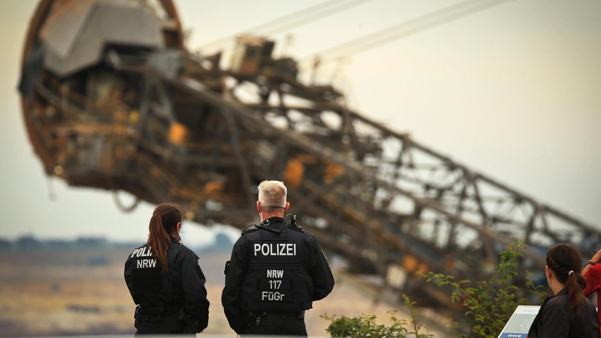 2 Polizisten stehen vor einem großen Braun-Kohle-Bagger. 
