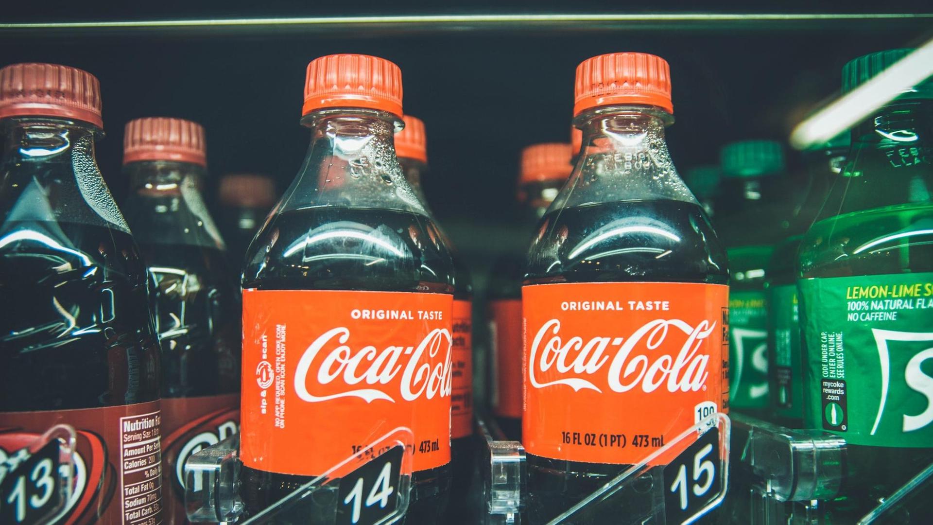 Verschiedene Flaschen, u.a. von Coca-Cola, stehen in einem Regal zum Verkauf.