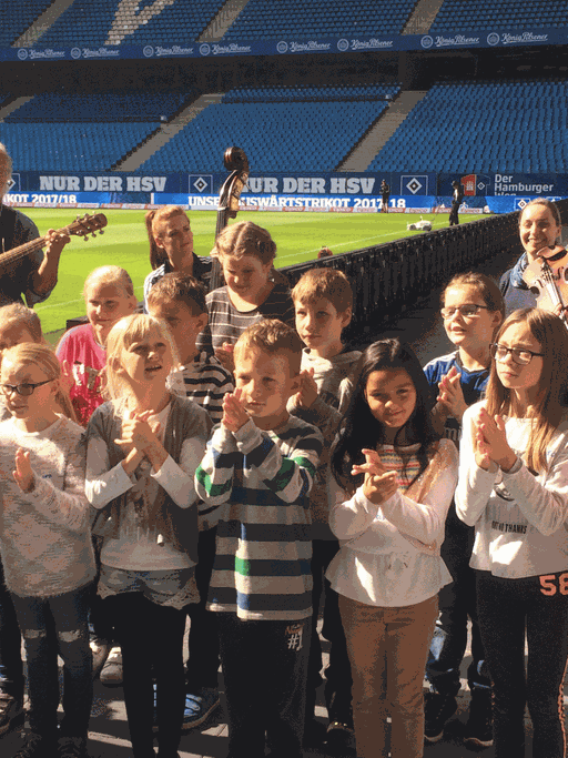 Die Symphoniker Hamburg kommen mit einigen Musikern regelmäßig ins Volksparkstadion, um dort mit Kindern aus bildungsfernen Familien eine Vereinshymne für den HSV zu komponieren.