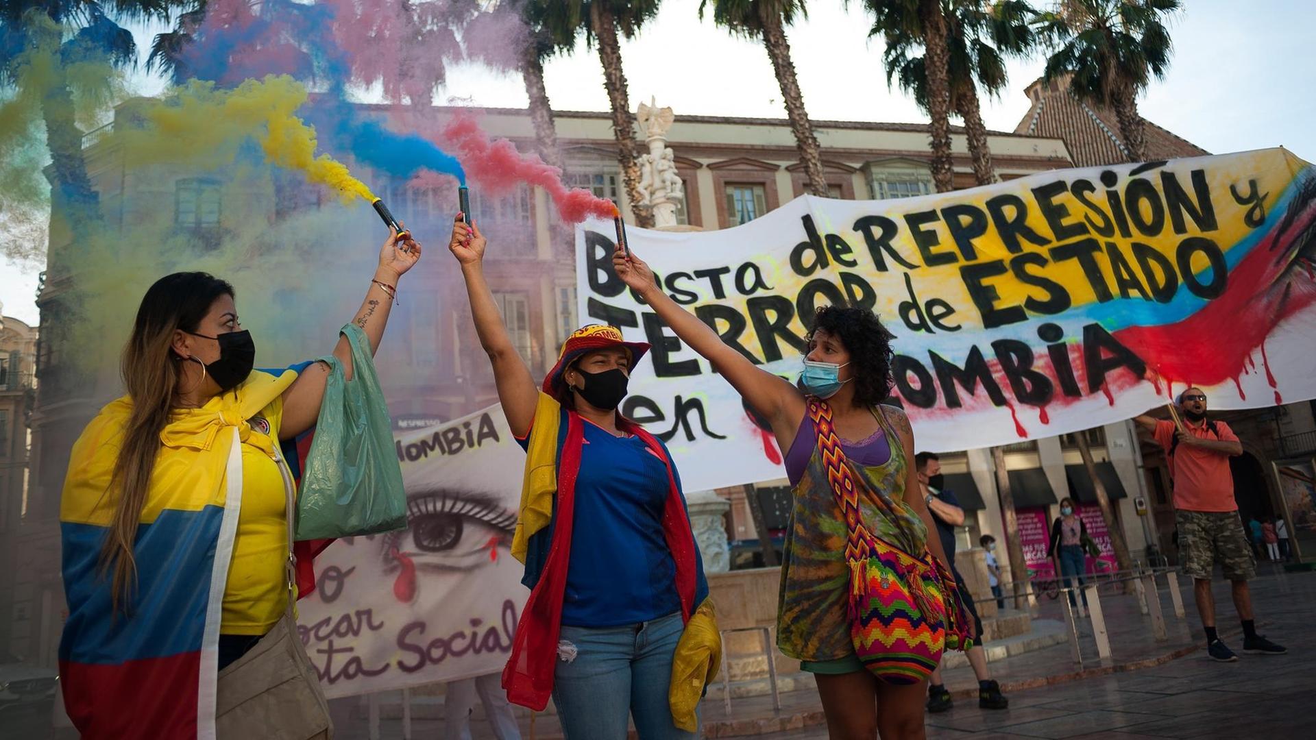 Drei Demonstrantinnen, die aus Kolumbien stammen, protestieren in der spanischen Stadt Málaga gegen die Regierung ihres Landes