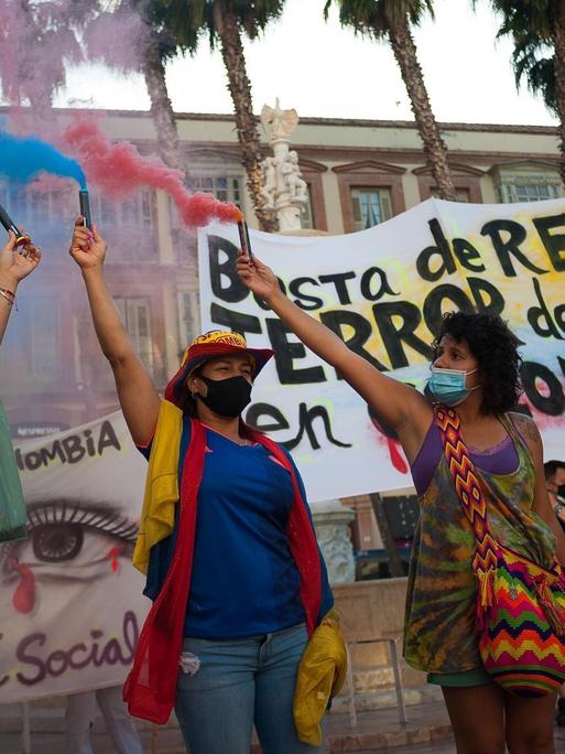Drei Demonstrantinnen, die aus Kolumbien stammen, protestieren in der spanischen Stadt Málaga gegen die Regierung ihres Landes