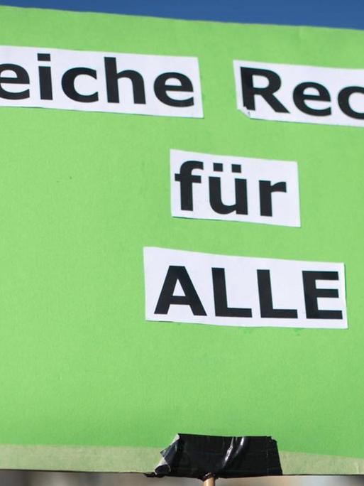 Hellgrünes Schild einer Demonstrantin mit den aus einer Zeitung ausgeschnittenen und aufgeklebten Worten: "Gleiche Rechte für ALLE !"