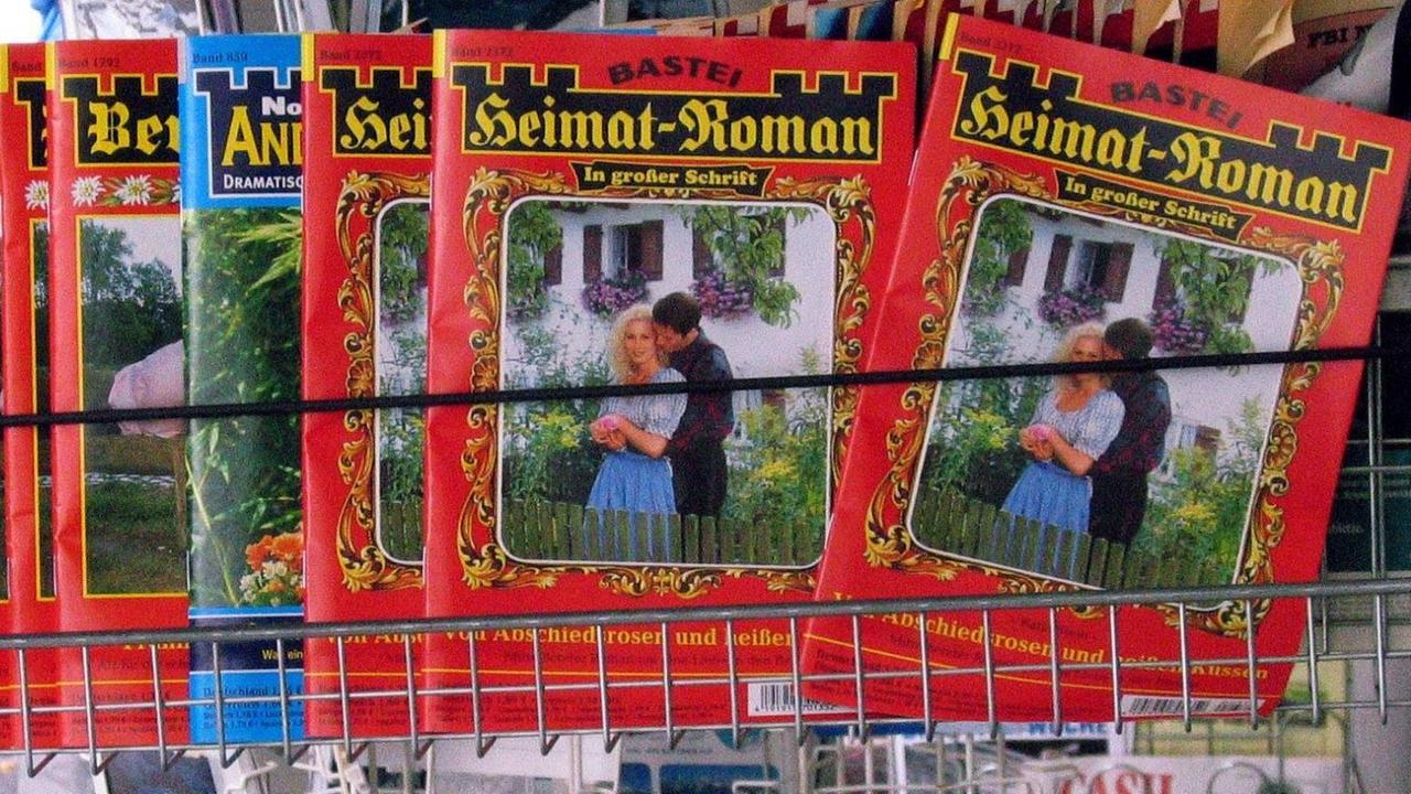 Diverse Printprodukte in der Auslage eines Kiosks, wo insbesondere die Reihe "Heimat-Roman" das Angebot bestimmt, darunter sind weitere Magazine zu sehen.