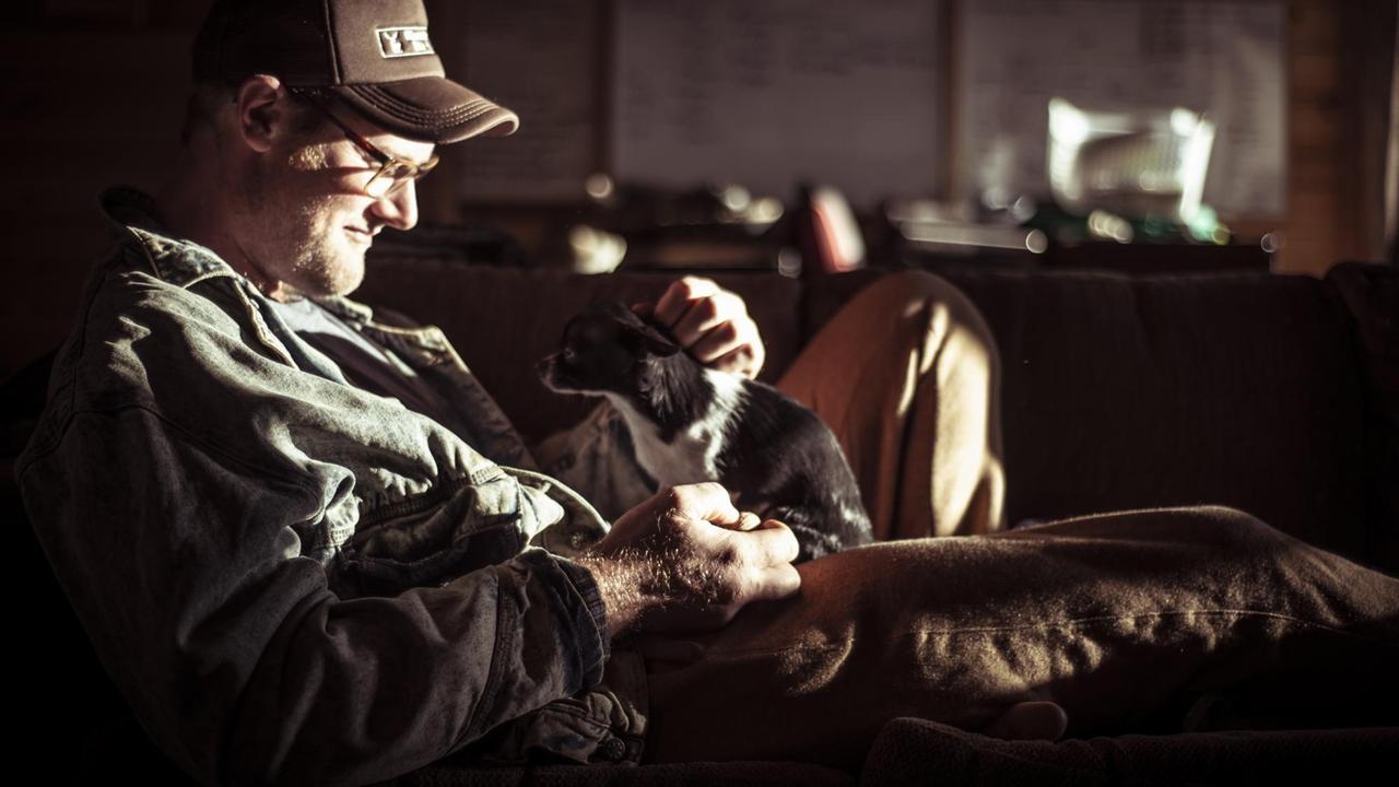 Farmer streichelt seinen kleinen Hund, der auf seinem Schoß sitzt.

