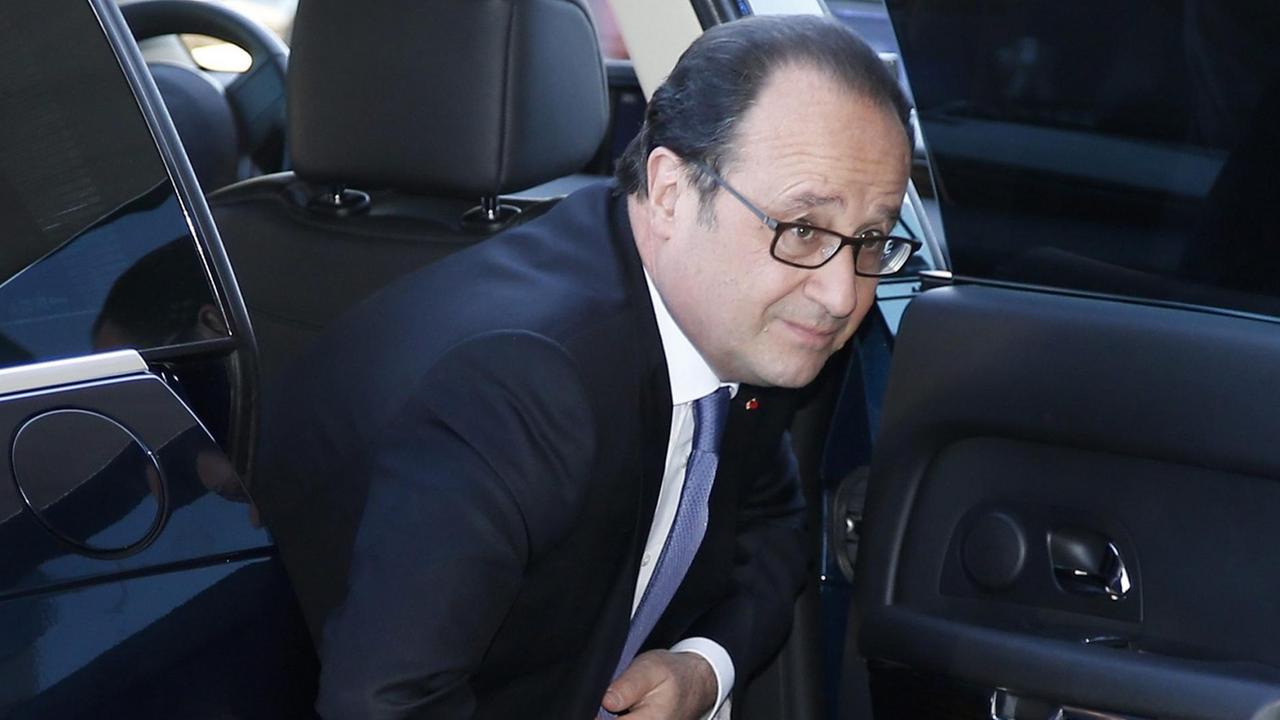 Hollande steigt im schwarzen Anzug mit blauer Krawatte aus einem Auto.